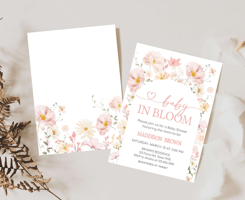 Floral baby shower invitation on a light surface with dried leaves.