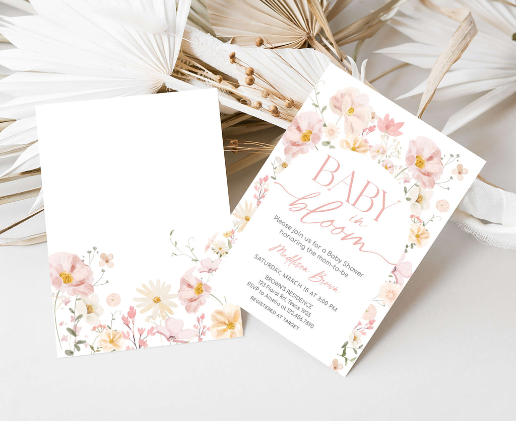 Floral baby shower invitation on a white surface with dried leaves.