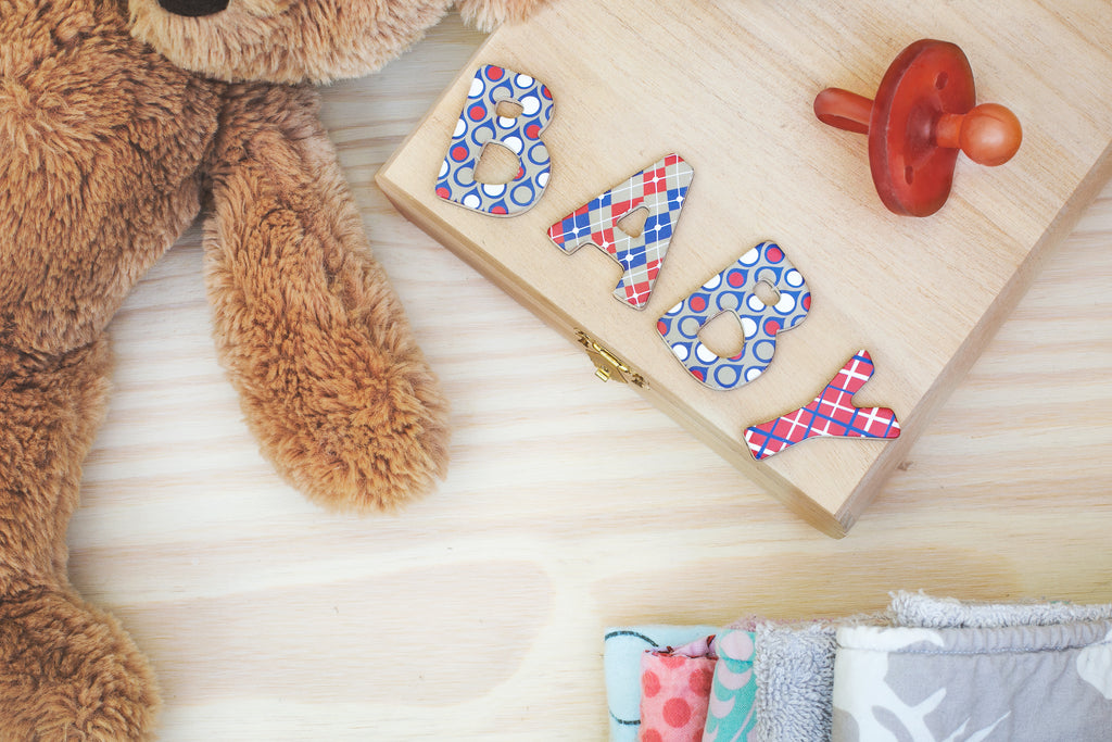 Teddy bear beside letter wood blocks spelled "BABY" and red pacifier